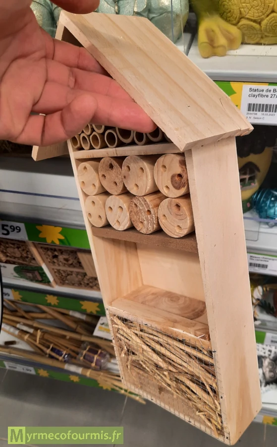 Un hôtel à insecte fait en bois non traité contenant des tiges creuses trop courtes pour abriter les insectes, tenu par une main dans un magasin.